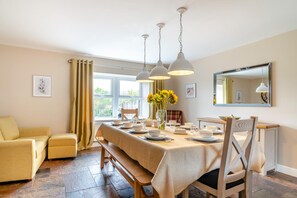 A dining area with a table set for four, a bench, a sofa, and a window with curtains.