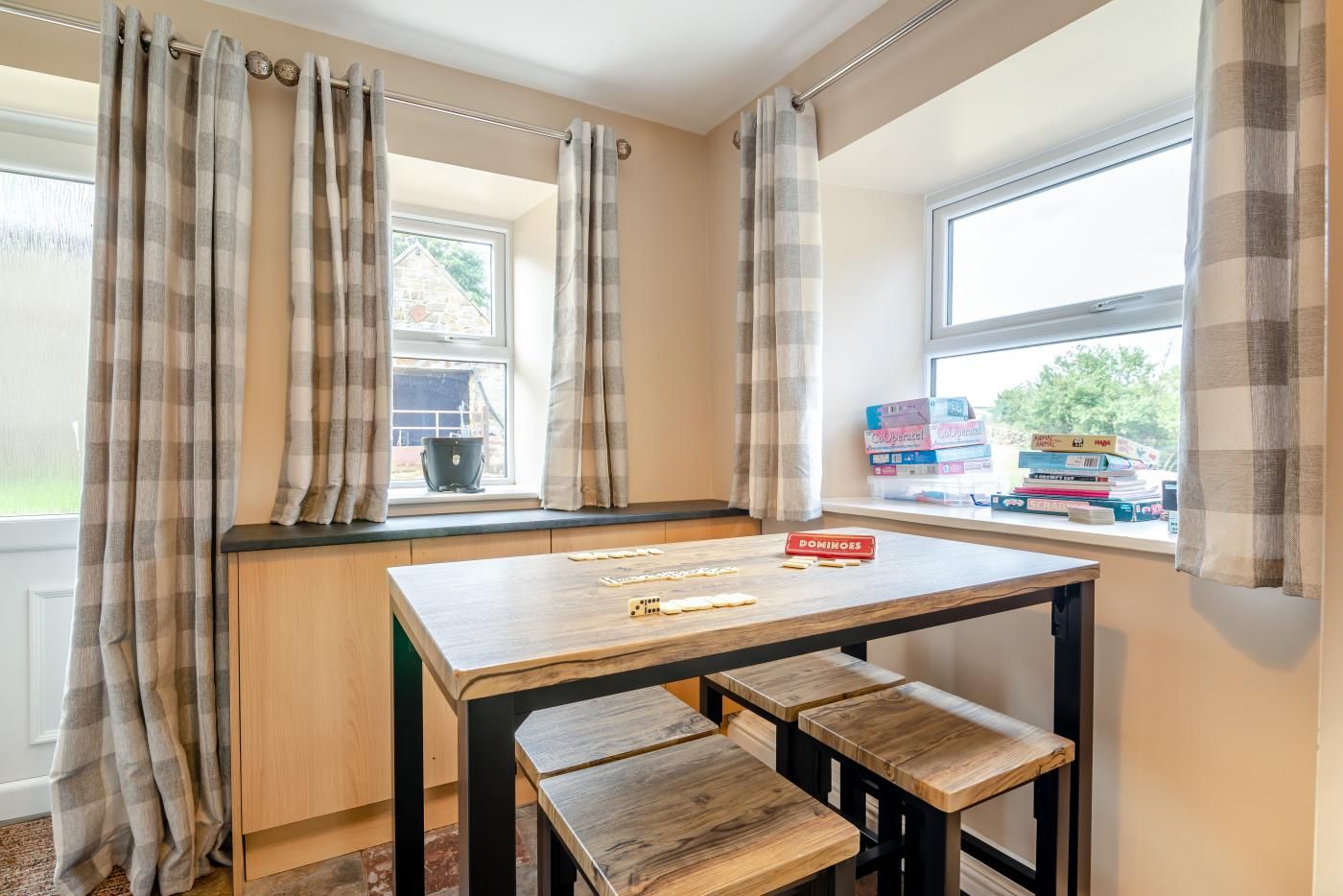 Quarto com mesa de madeira, bancos, janela com cortinas e vista para o exterior.