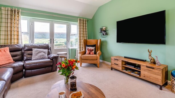 A living room with a sofa, armchair, coffee table, and a flat-screen TV mounted on the wall.