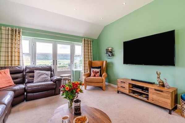 A living room with a sofa, armchair, coffee table, and a flat-screen TV mounted on the wall.