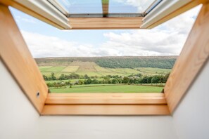 Een dakraam met uitzicht op een groen landschap en verre heuvels.
