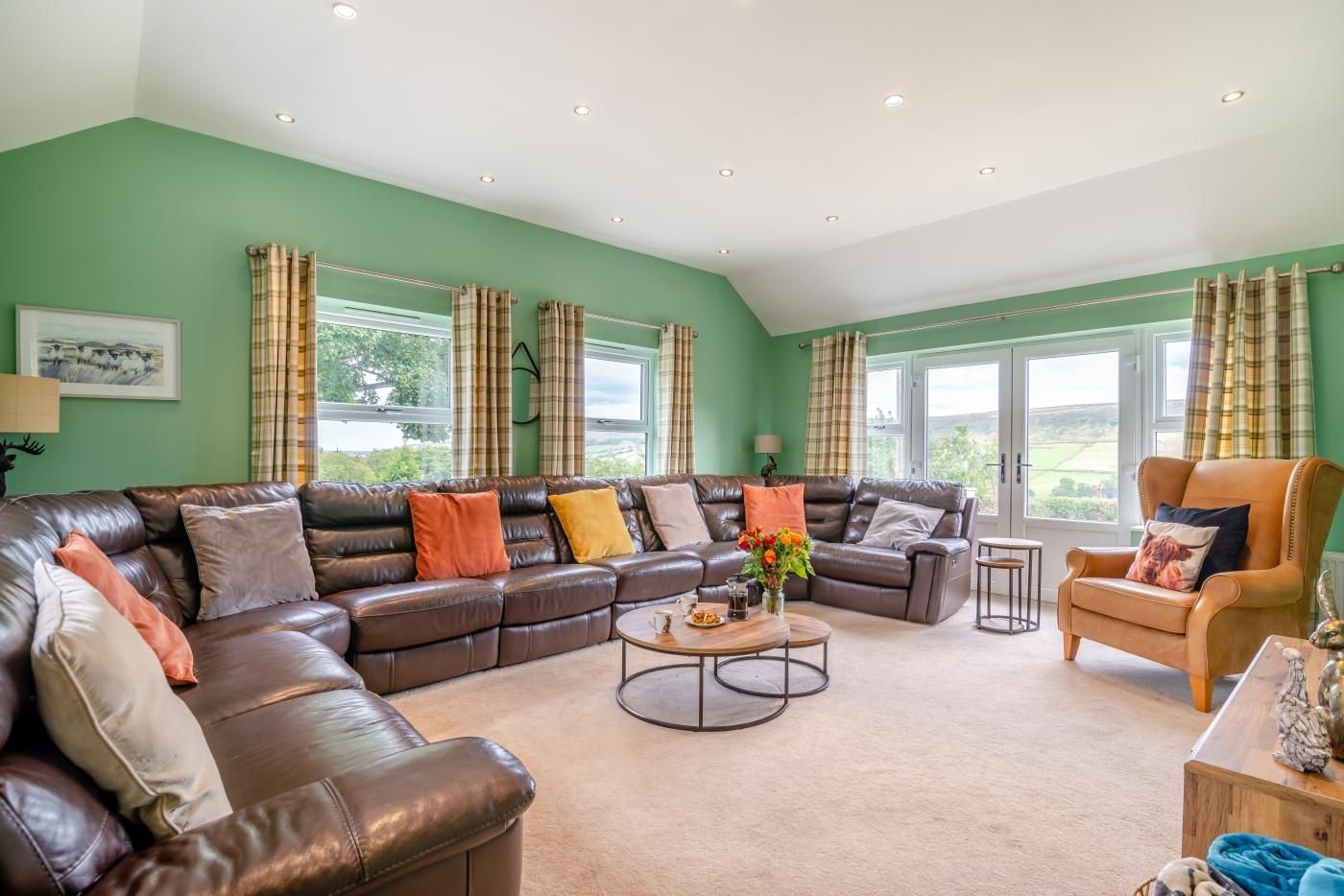 A spacious living room with a large leather sofa, a wooden coffee table, and a leather armchair.