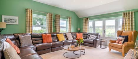 A spacious living room with a large leather sofa, a wooden coffee table, and a leather armchair.