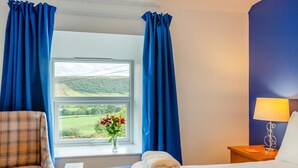 A hotel room with a bed, a chair, a nightstand, a lamp, and a window with curtains.