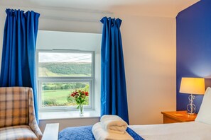 A hotel room with a bed, a chair, a nightstand, a lamp, and a window with curtains.