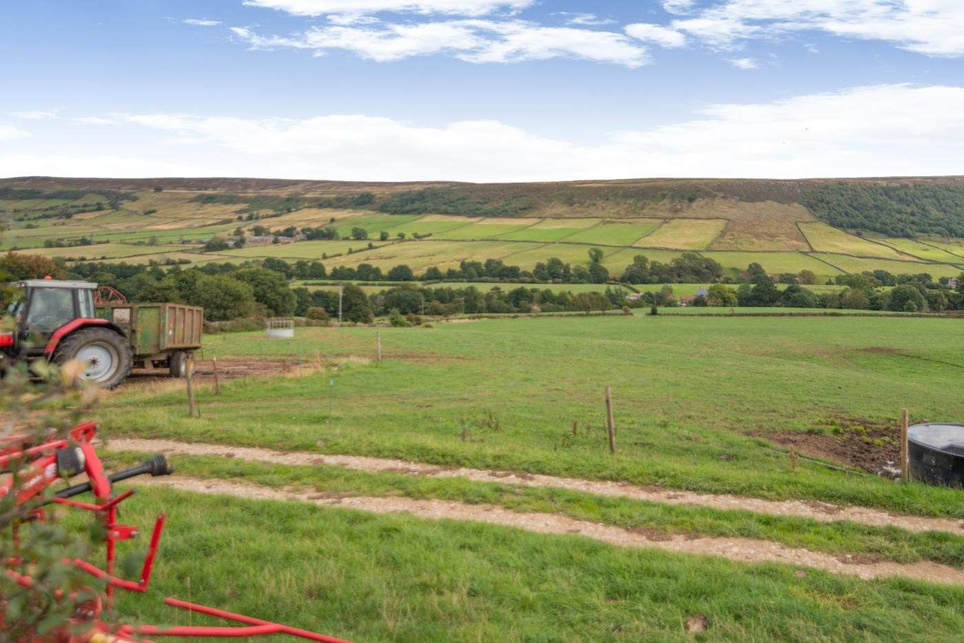 A rural landscape with a tractor and a trailer, a fenced field, and rolling hills in the background.