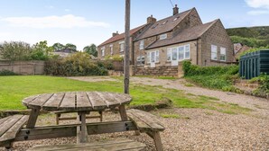 A stone house with a gravel driveway and a wooden picnic table in the foreground.