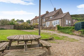 A stone house with a gravel driveway and a wooden picnic table in the foreground.