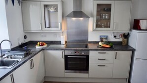 Une cuisine moderne équipée d’un four en acier inoxydable, d’un micro-ondes encastré et d’une cuisinière à gaz. On y trouve un évier avec un égouttoir, ainsi que des placards au-dessus du plan de travail.