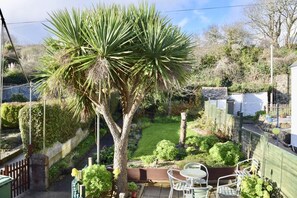 A garden with a large palm tree, a paved patio with metal chairs, and a white fence. - 3 Bed in Marazion (oc-smccbl) (Marazion)