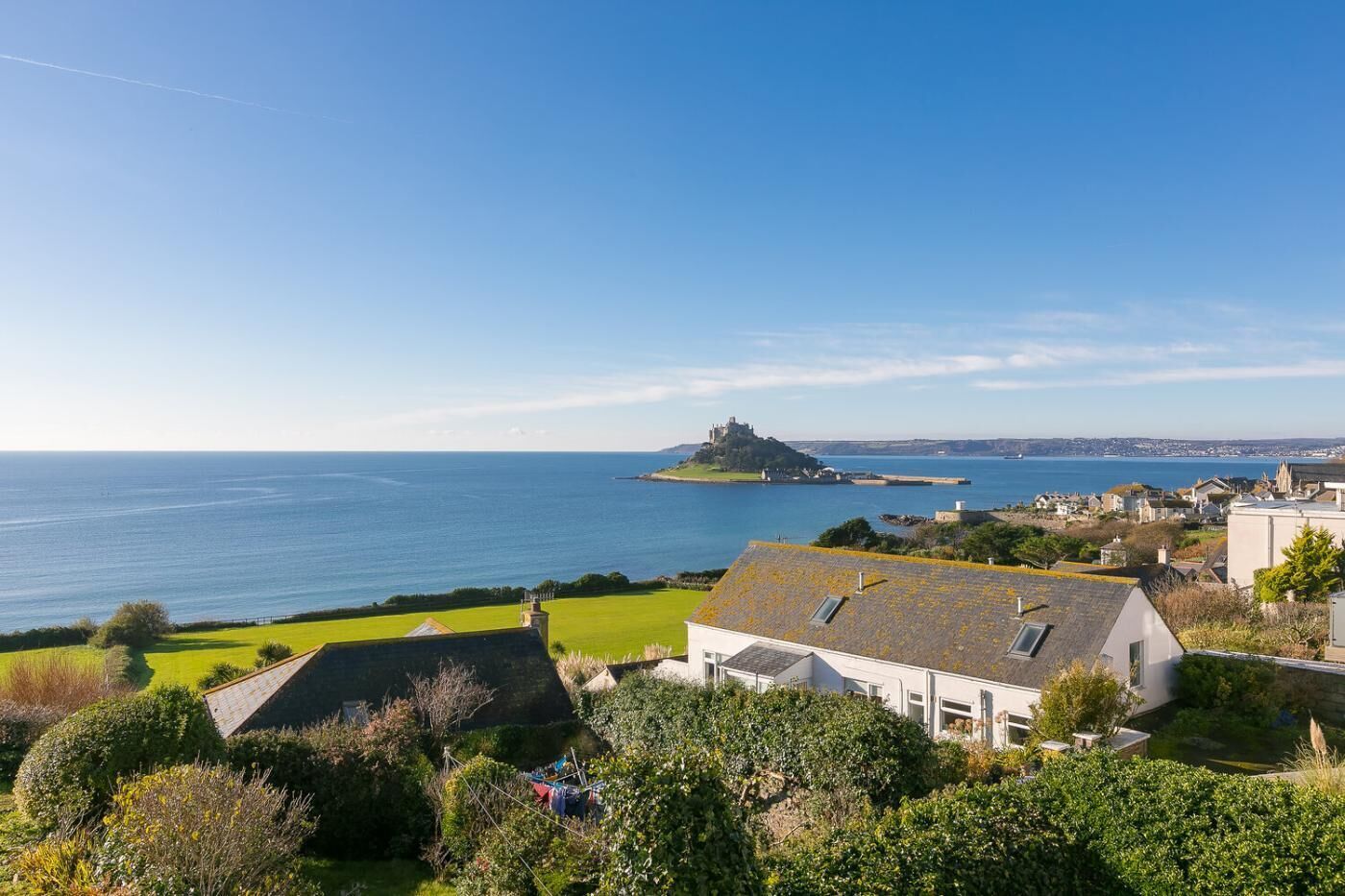 A coastal town with a prominent castle on a small island, surrounded by residential buildings and lush greenery.