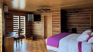 A wooden cabin room with a bed, a desk, and a television.