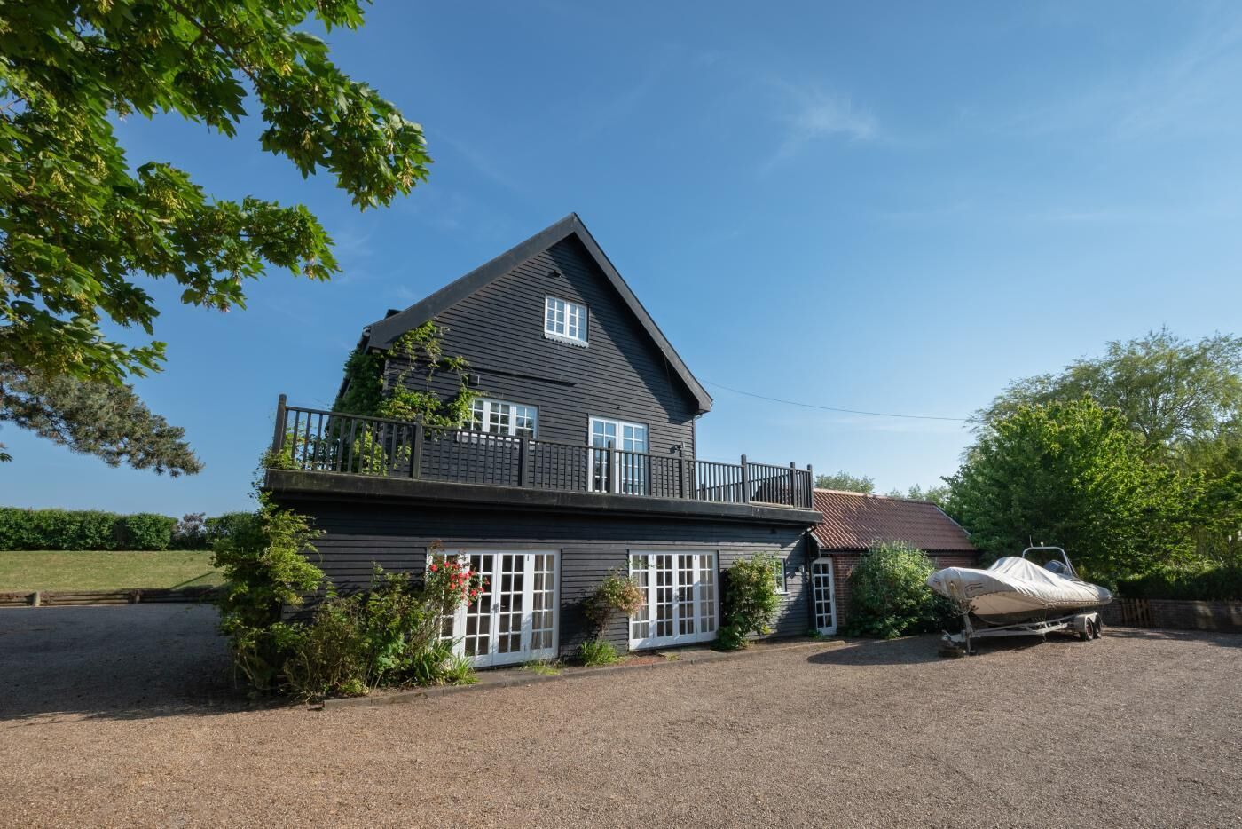 A two-story house with a balcony, a covered boat, and a gravel driveway.