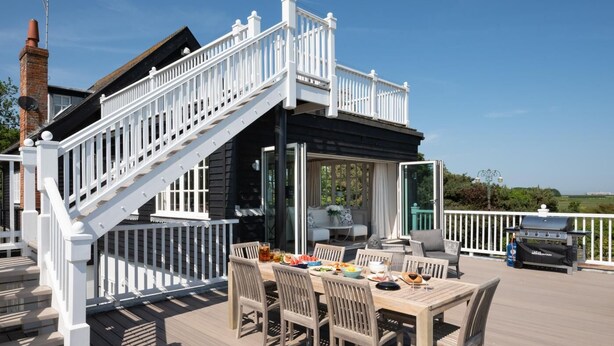 Une terrasse dotée d’un espace repas, d’un barbecue extérieur et d’un escalier menant à une zone abritée.