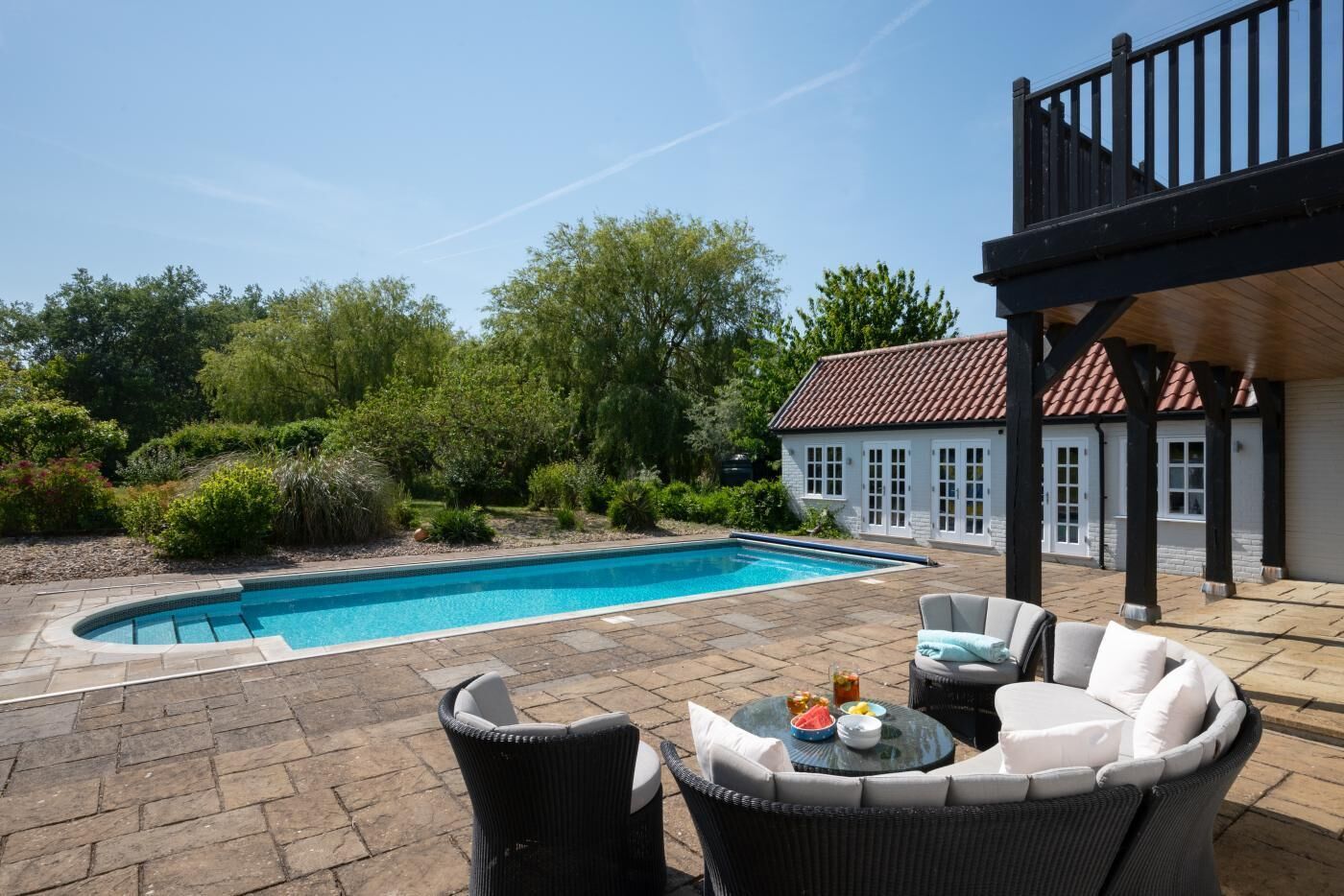 A backyard with a swimming pool, outdoor furniture, and a house with a red-tiled roof.