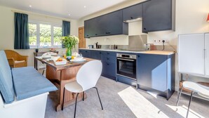 A modern kitchen with dark cabinets, a built-in oven, and a dining area with a table and chairs. - 2 Bed in Kettlestone (oc-t32268) (Little Snoring)