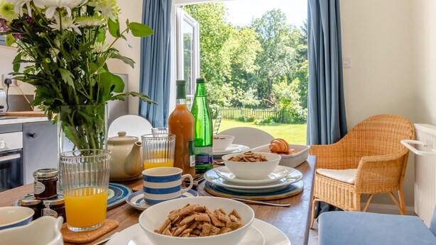A breakfast setup with a table, breakfast items, a vase of flowers, and a view of the outdoors. - 2 Bed in Kettlestone (oc-t32268) (Little Snoring)