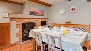 A cozy breakfast setup with a brick fireplace, wooden beams, and a table set for breakfast. - 4 Bed in Wells-next-the-Sea (oc-2045) (Wells-next-the-Sea)