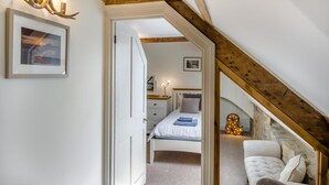 Une chambre avec un plafond en pente, un lit recouvert d’une couverture bleue, une table de chevet avec une lampe et un lustre décoratif en forme de bois de cerf.