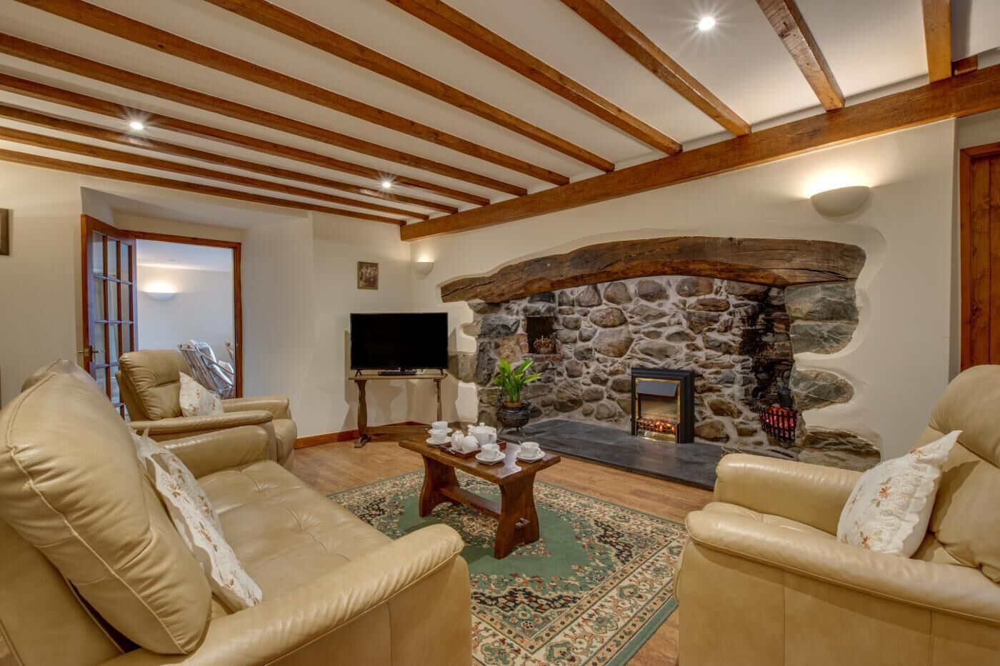 A cozy living room with a stone fireplace, leather sofas, a coffee table, and a television.