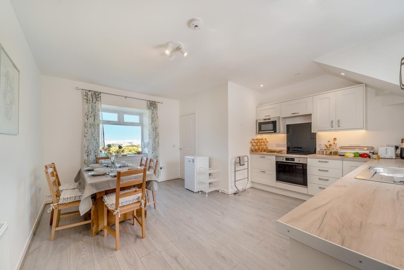 A modern kitchen with white cabinets, a built-in oven, and a dining area with a table set for four.
