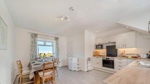 A modern kitchen with white cabinets, a built-in oven, and a dining area with a table set for four. - 3 Bed in Clachan (oc-h32242) (Clachan)