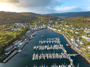 Vista aérea de un pueblo costero con un puerto deportivo, casas y colinas al fondo.