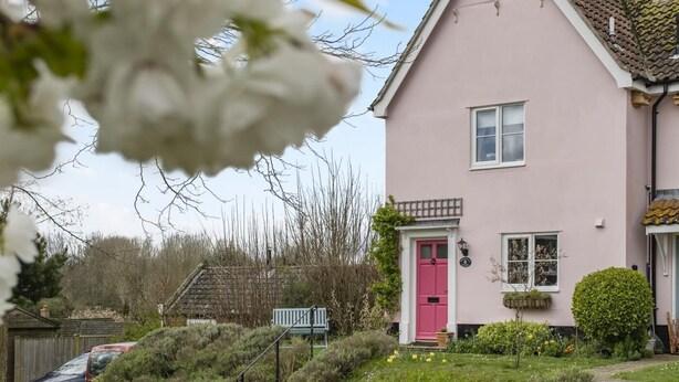 Una casa rosa con una porta rossa, un piccolo giardino e una panchina.
