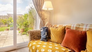 Un accogliente soggiorno con divano, lampada e vista su un giardino attraverso una porta in vetro.