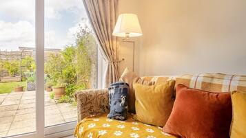 A cozy living room with a sofa, a lamp, and a view of a garden through a glass door.