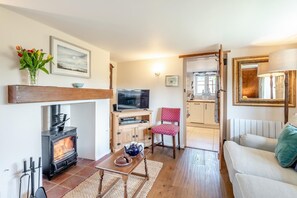 Ein gemütliches Wohnzimmer mit Kamin, Fernseher, Esstisch mit Stuhl und einer Couch.