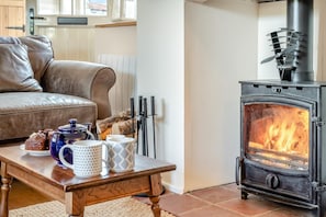 Ein gemütliches Wohnzimmer mit einem Ledersofa, einem Holztisch mit Tassen und Kuchen sowie einem Kaminofen.