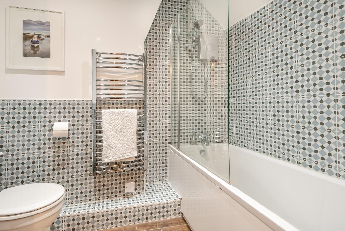Ein Badezimmer mit gemusterten Fliesen, einer Duschkabine aus Glas, einer Toilette und einem gerahmten Bild an der Wand.