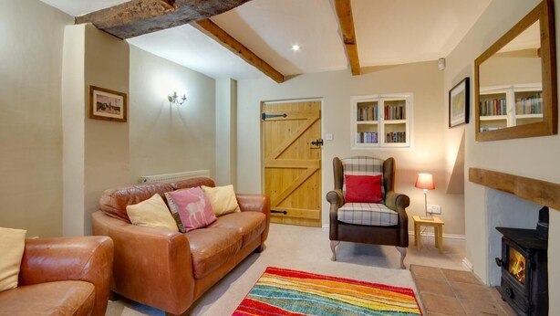 Una sala de estar acogedora con un sofá de cuero, un sillón a cuadros, una alfombra colorida, una estantería y una chimenea.