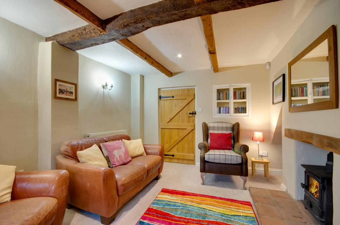 Una sala de estar acogedora con un sofá de cuero, un sillón a cuadros, una alfombra colorida, una estantería y una chimenea.