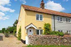 A two-story house with a yellow facade, a white door, and a stone wall in front. - 3 Bed in Brinton (oc-2061) (Sharrington)