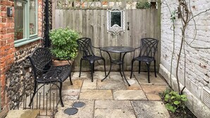 Une terrasse avec une table et quatre chaises, un pot de fleurs, une clôture en bois et un mur en briques.