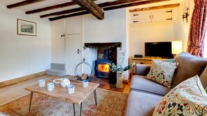 Un salon chaleureux avec des poutres apparentes, une cheminée, un canapé, un téléviseur et une table à manger avec des tasses.