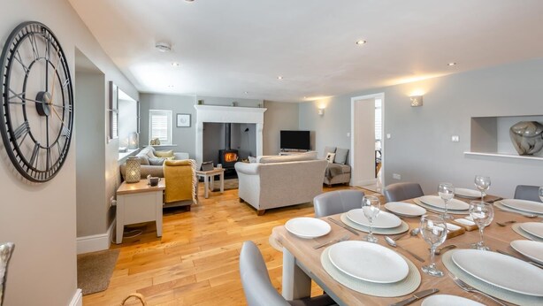 Un salon moderne avec une cheminée, un coin repas avec des tables dressées et une grande horloge murale.