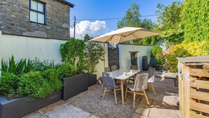 Un bâtiment en pierre avec une fenêtre, une terrasse avec une table et des chaises, et une structure en bois.