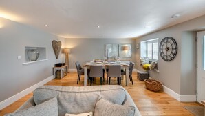 Un coin repas avec une table dressée pour quatre personnes, un canapé au premier plan et une horloge murale.