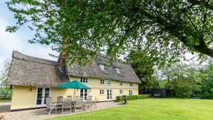 A thatched-roof house with a patio area, a green umbrella, and a well-maintained lawn. - 5 Bed in Finningham (oc-obhf) (Finningham)