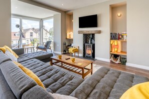 A modern living room with a large sofa, a fireplace, a flat-screen TV, and a bookshelf. - 4 Bed in Mumbles (oc-t32236) (The Mumbles)