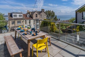 A balcony with a table set for breakfast, overlooking a residential area and the sea. - 4 Bed in Mumbles (oc-t32236) (The Mumbles)
