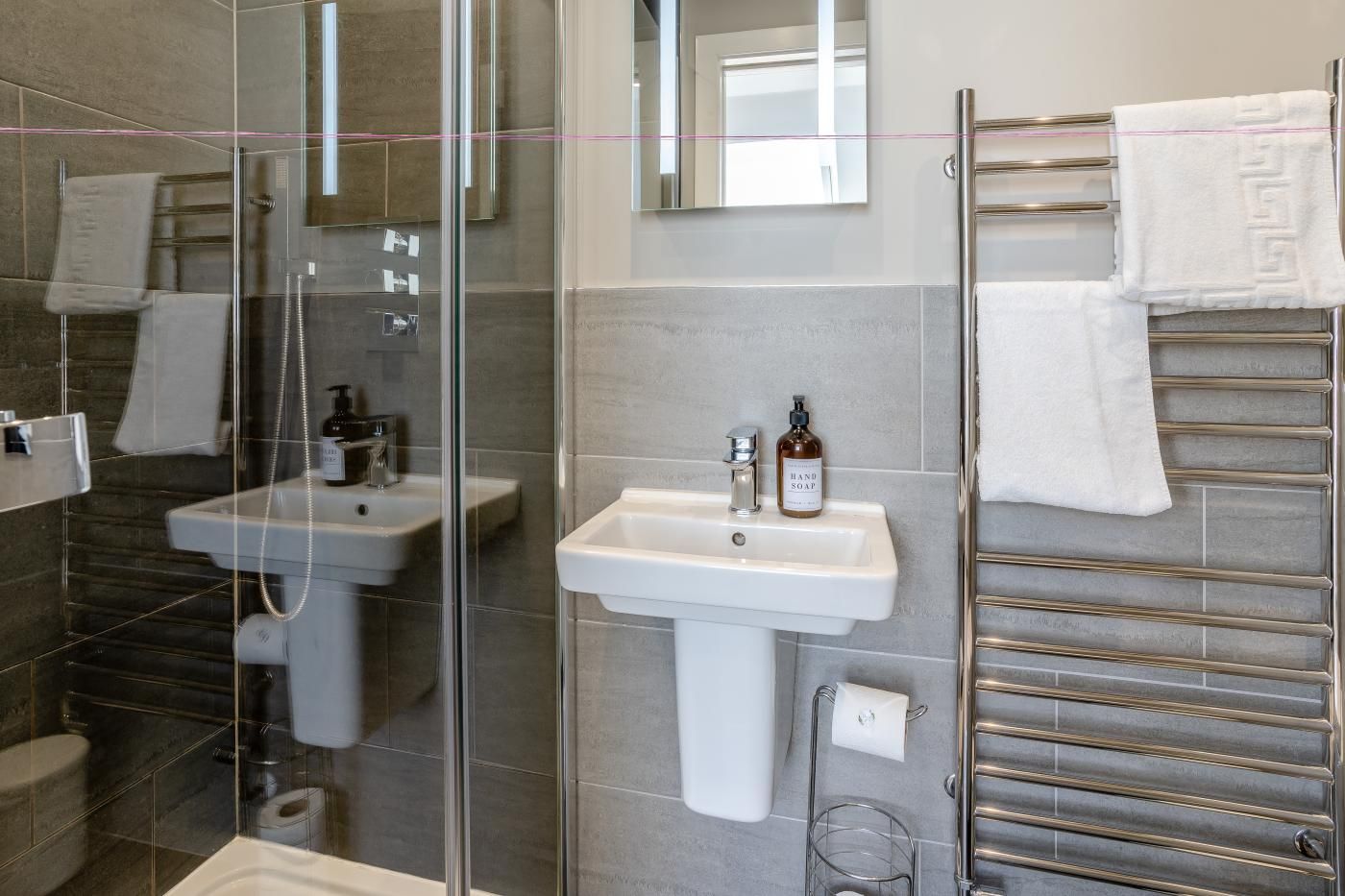 A modern bathroom with a glass shower enclosure, a white sink with a soap dispenser, and a towel rack with multiple towels.
