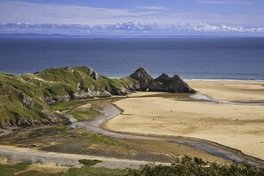 A coastal landscape with a sandy beach, rocky outcrops, and a clear view of the sea. - 4 Bed in Mumbles (oc-t32236) (The Mumbles)