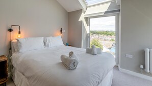 Ein Schlafzimmer mit einem großen Bett, einem Oberlicht, Blick ins Freie und einem Nachttisch mit Lampe.