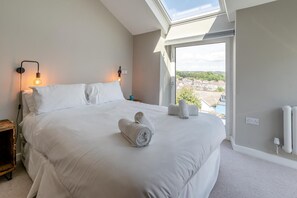 A bedroom with a large bed, a skylight, a view of the outside, and a bedside table with a lamp. - 4 Bed in Mumbles (oc-t32236) (The Mumbles)