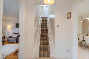A staircase with striped carpet, a dining area with white chairs, and a living room with a sofa and lamp. - 4 Bed in Walberswick (oc-pemb) (Walberswick)