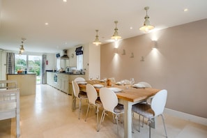 A modern kitchen with a dining area, featuring a wooden table, white chairs, and pendant lighting. - 4 Bed in Walberswick (oc-pemb) (Walberswick)